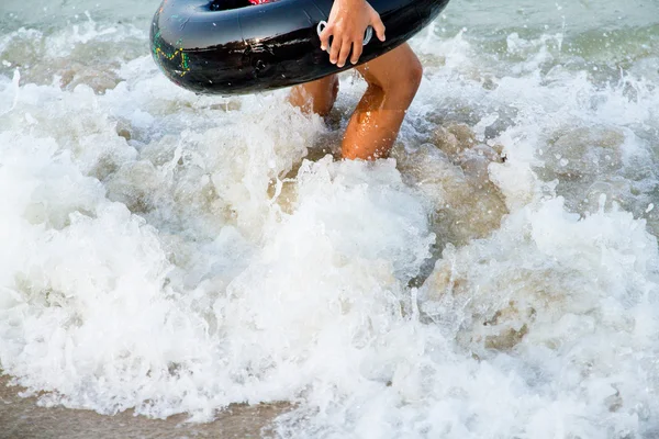 Un niño sostiene una boya anular negra caminando sobre el mar . — Foto de Stock