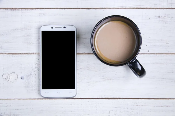 Smartphone e xícara de café no fundo de madeira branca . — Fotografia de Stock