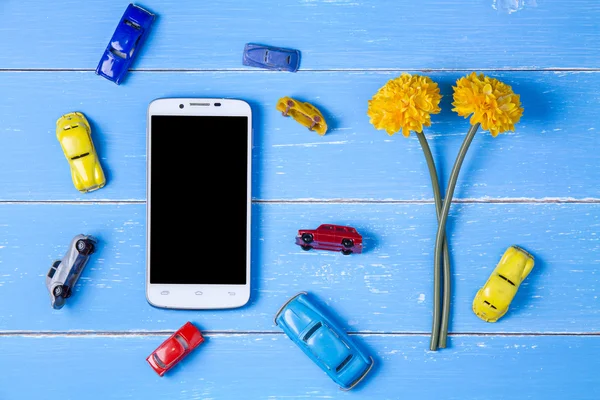 Telefone inteligente, brinquedos carro e flores de plástico no bac de madeira azul — Fotografia de Stock