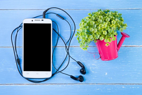 Telefone inteligente e flores de plástico no fundo de madeira azul . — Fotografia de Stock