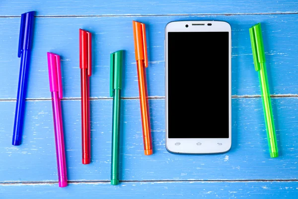 Telefone inteligente e caneta colorida no fundo de madeira azul — Fotografia de Stock