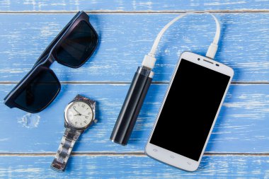 Akıllı telefon, güneş gözlüğü, taşınabilir pil ve mavi ahşap üzerine izle