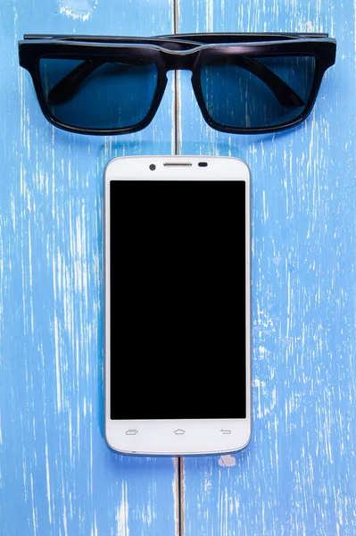 Telefone inteligente e óculos de sol em fundo de madeira azul — Fotografia de Stock