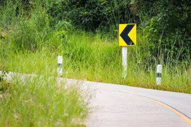 Trafik işaretleri sola ve dümdüz bir viraja işaret ediyor. Kırsal alanda bir sıra çimen. Ana konunun dışında. .