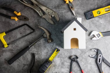 Ahşap beyaz ev oyuncakları ve inşaat aletleri. Gri-siyah çimento zemin zemininde kopya alanı var. Emlak konsepti, yeni ev onarım konsepti.