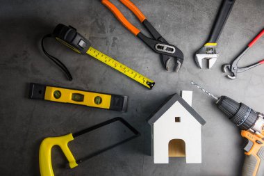 Ahşap beyaz ev oyuncakları ve inşaat aletleri. Gri-siyah çimento zemin zemininde kopya alanı var. Emlak konsepti, yeni ev onarım konsepti.