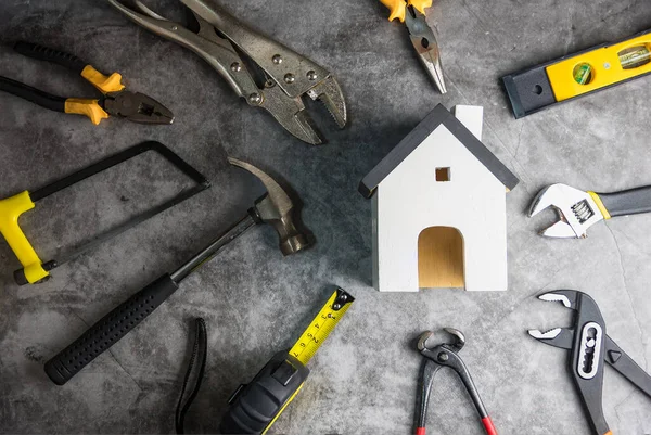 Ahşap beyaz ev oyuncakları ve inşaat aletleri. Gri-siyah çimento zemin zemininde kopya alanı var. Emlak konsepti, yeni ev onarım konsepti.