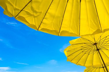Kumsaldaki sarı şemsiye ve mavi gökyüzü yazları tatili simgeliyor. Tayland.
