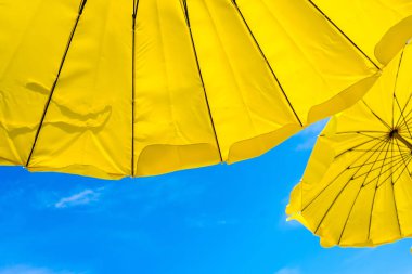 Kumsaldaki sarı şemsiye ve mavi gökyüzü yazları tatili simgeliyor. Tayland.