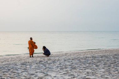 Prachuap Khiri Khan, Thailand- April, 04, 2021 : Sunrise with reflection on the sea and beach that have blurred silhouette photo of buddhist monk walking alms offering food in the morning on beach of Thailand.