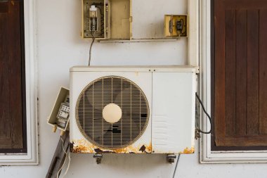 Duvara monte edilmiş havalandırma ünitesi görünür bir boru ve ahşap panel arka planı olan bir binaya bağlı.