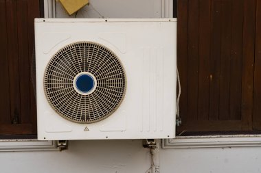 Duvara monte edilmiş havalandırma ünitesi görünür bir boru ve ahşap panel arka planı olan bir binaya bağlı.