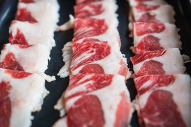 Yakın plan kesilmiş et ya da domuz eti. Sıcak tencere pişirmeye ya da Kore barbeküsüne hazır siyah bir tepside dizilmiş.