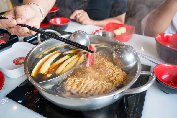 İnsanlara yakın çekim erişte, sebze ve çiğ et ile sıcak tencerenin tadını çıkarırken bir restoran masasında bölünmüş et suyunda pişirilir.