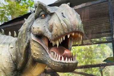 Ağaçlar ve bitki örtüsüyle çevrili bir açık hava parkında gerçek boyutta Tyrannosaurus Rex dinozor kopyası.
