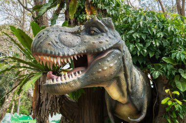 Ağaçlar ve bitki örtüsüyle çevrili bir açık hava parkında gerçek boyutta Tyrannosaurus Rex dinozor kopyası.
