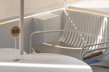 Beyaz metal koltuğu ve yumuşak doğal ışıkla yıkanmış masası olan boş, modern bir açık hava oturma alanı.