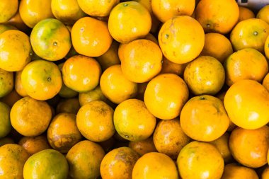 Değişen dokuları ve doğal kusurları olan olgun sarı ve yeşil portakal yığını.