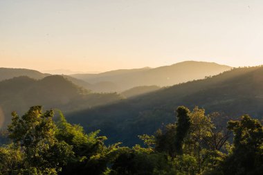 Scenic view of misty forested mountains at sunrise with layers of rolling hills covered in dense green foliage