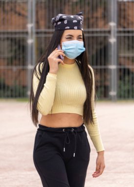 Ameliyat maskeli bir kız cep telefonuyla konuşuyor ve basketbol sahasında yürüyor.