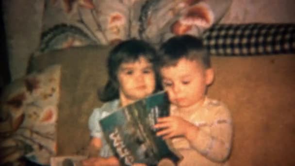 Toddler chłopiec i dziewczyna, czytanie czasopism na kanapie — Wideo stockowe