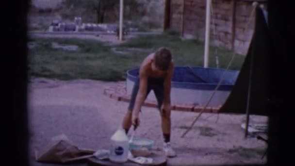 Niño en un campamento agitando una olla cerca de una fogata abierta — Vídeo de stock