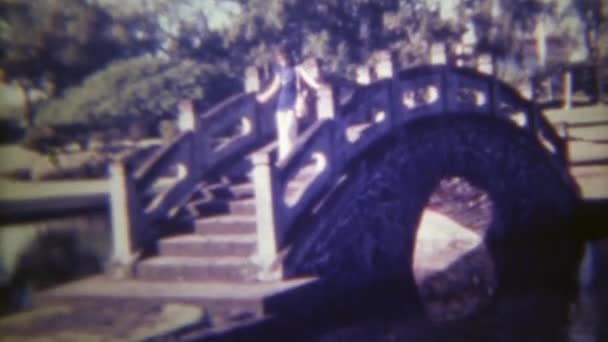 Frauen überqueren Gartenbrücke über Wasser — Stockvideo