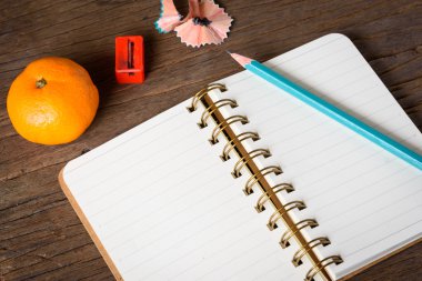 Eski ahşap masa üstünde açılan bir defter kalem ve kalemtıraş.