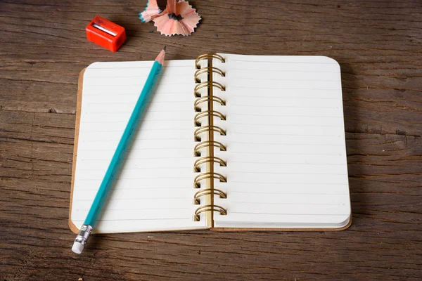 An opened notebook with pencil and Pencil Sharpener on old wooden table. — Stock Photo, Image