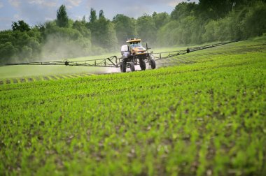 Tractor sprinkling young plants from pests at a farmer's field. clipart
