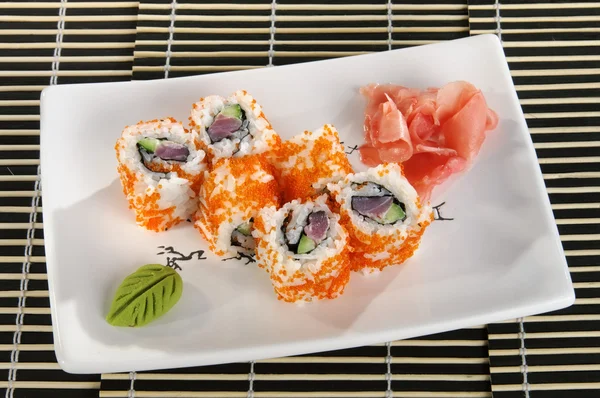 Sushi menu: a set of rolls with flying fish roe and avocado with wasabi and ginger on a plate — Stock Photo, Image