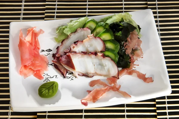 Sushi menu: sliced octopus with slices of cucumber and seaweed on a plate — Stock Photo, Image