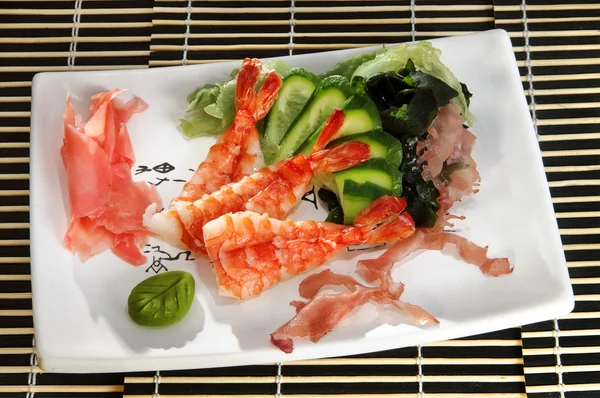Sushi menu: shrimp with slices of cucumber and seaweed on a plate — Stock Photo, Image