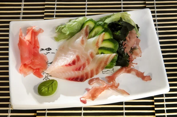 Sushi menu: sliced fish with slices of cucumber and seaweed on a plate — Stock Image Sushi menu: sliced fish with slices of cucumber and seaweed on a plate Stock Photo