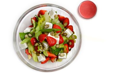 Salad in pozrachnoy plate with strawberries, sunflower seeds, cheese, greens and sauce. On a white background. clipart