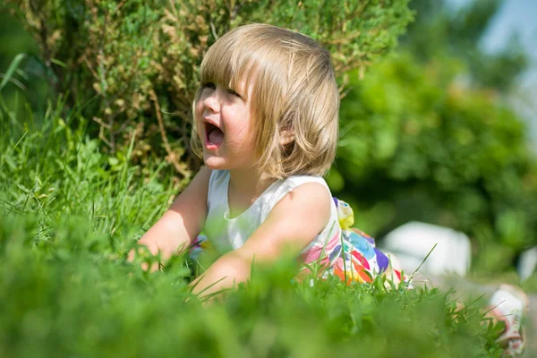 Liten flicka i en park på gräset och föll ner gråt. — Stockfoto