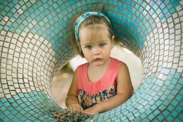 Маленькая девочка с повязкой на голове в игре круглая фигура на детской площадке, играющая с песком . — стоковое фото