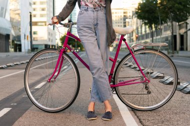 Şehirde bisiklet yolunda pembe retro bisikletli tanınmayan genç bir kadın. Aktif yaşam tarzı ve sürdürülebilir hareketlilik kavramı.