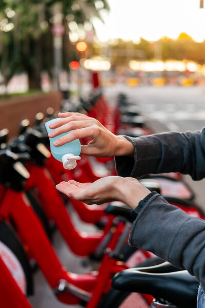 vertical photo of hands washing with disinfectant gel next to an urban bicycle rental parking, concept of protection against covid and sustainable mobility