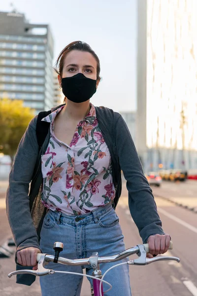 vertical portrait of a young girl with protective mask at the city riding a pink retro bike, concept of active lifestyle, protection against covid and sustainable mobility