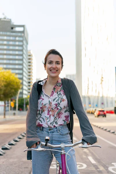 vertical portrait of a smiling young woman at the city riding a pink retro bicycle by the bike path, concept of active lifestyle and sustainable mobility
