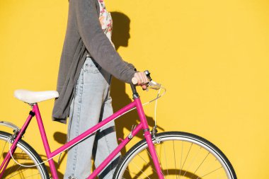 unrecognizable young woman walking with a pink retro bike in front of a colorful yellow wall, concept of active lifestyle and sustainable mobility, copy space for text