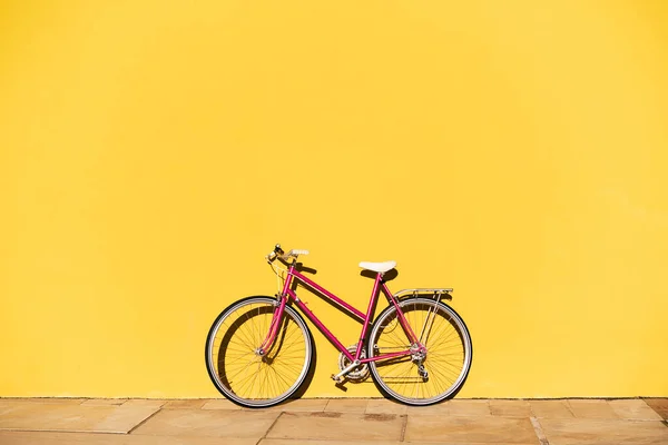 Renkli sarı bir duvarda desteklenen pembe retro bisiklet, aktif yaşam tarzı ve sürdürülebilir kentsel hareketlilik kavramı, metin için kopyalama alanı