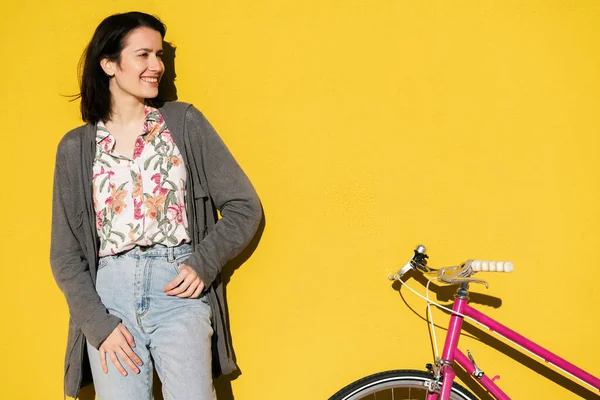 portrait of a happy young girl leaning against a colorful yellow wall next to her pink retro bike, concept of active lifestyle and sustainable mobility, copy space for text