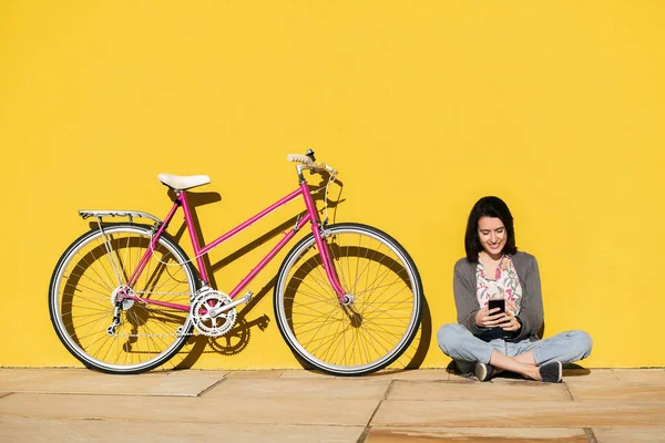 Menina Feliz Olhando Telefone Inteligente Sentado Lado Sua Bicicleta Encostada — Fotografia de Stock