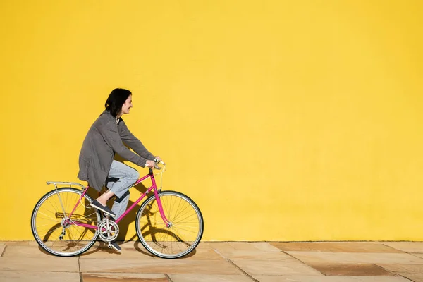 happy young girl smiles as she rides her retro pink bike along a colorful yellow wall, concept of active lifestyle and sustainable mobility, copy space for text