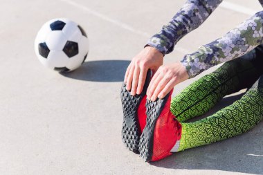 Beton bir futbol sahasında futbol topunun yanında oturan tanınmamış sporcu, şehirde sağlıklı yaşam tarzı ve şehir sporu kavramı, metin için yer kopyalama