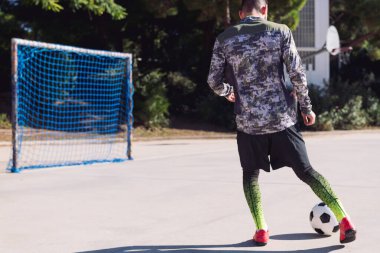 Tanınmayan bir futbolcunun, beton bir futbol sahasında futbol topunu boş bir kaleye atması, şehirde sağlıklı yaşam tarzı ve kentsel spor kavramı, metin için kopya alanı