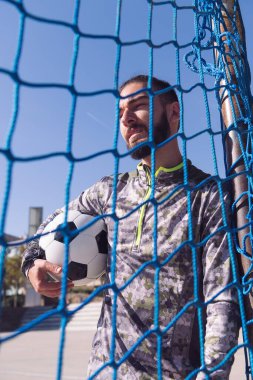 Kolunun altında futbol topu olan yakışıklı bir hippi sporcunun dikey portresi, şehirde sağlıklı yaşam tarzı ve şehir sporu kavramı, metin için yer kopyalama