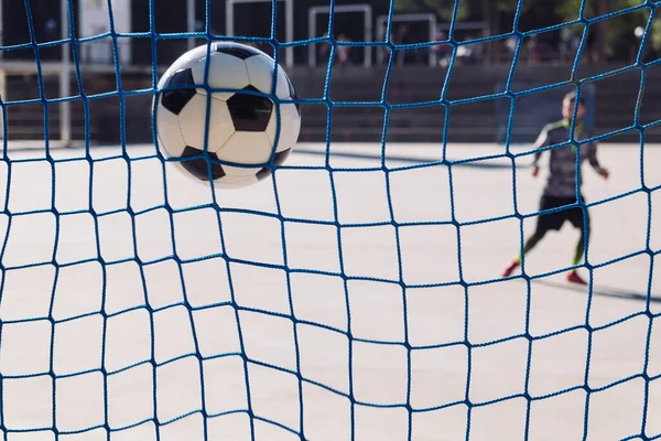 football ball hitting the goal net with an unfocused sportsman in the background, concept of healthy lifestyle and urban sport in the city, copy space for text